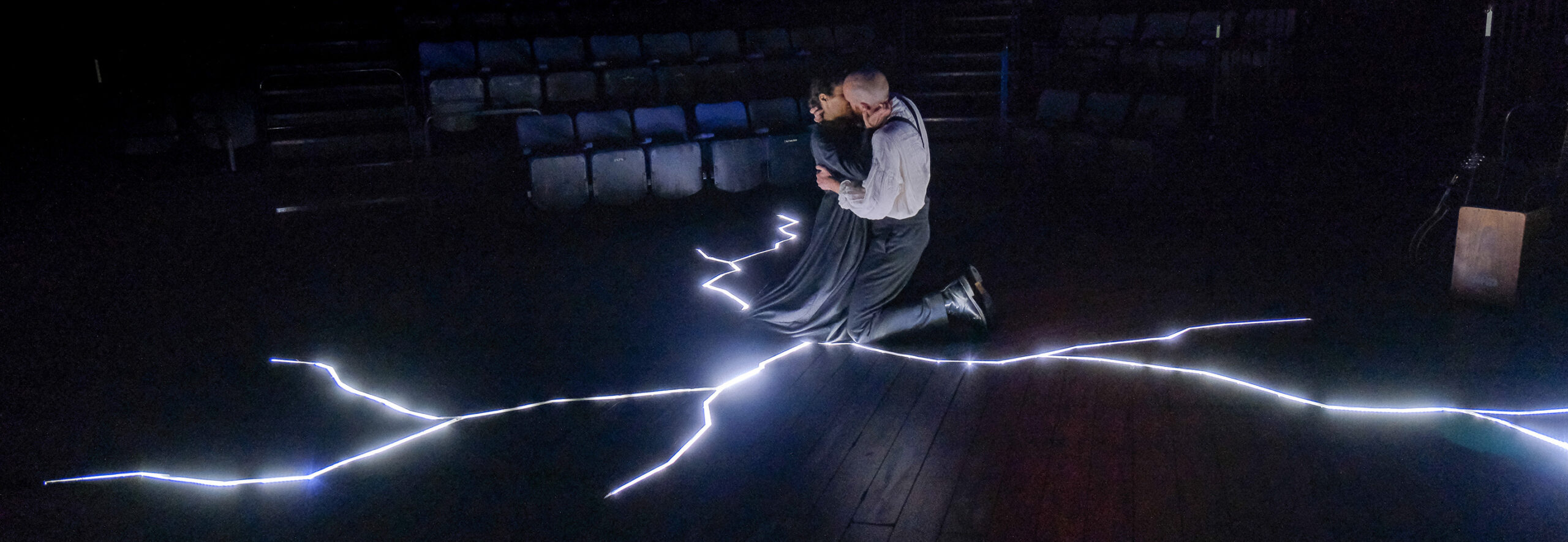 theatre performance image: Jane Eyre and Rochester embracing at the centre of a lightening bolt on the stage floor