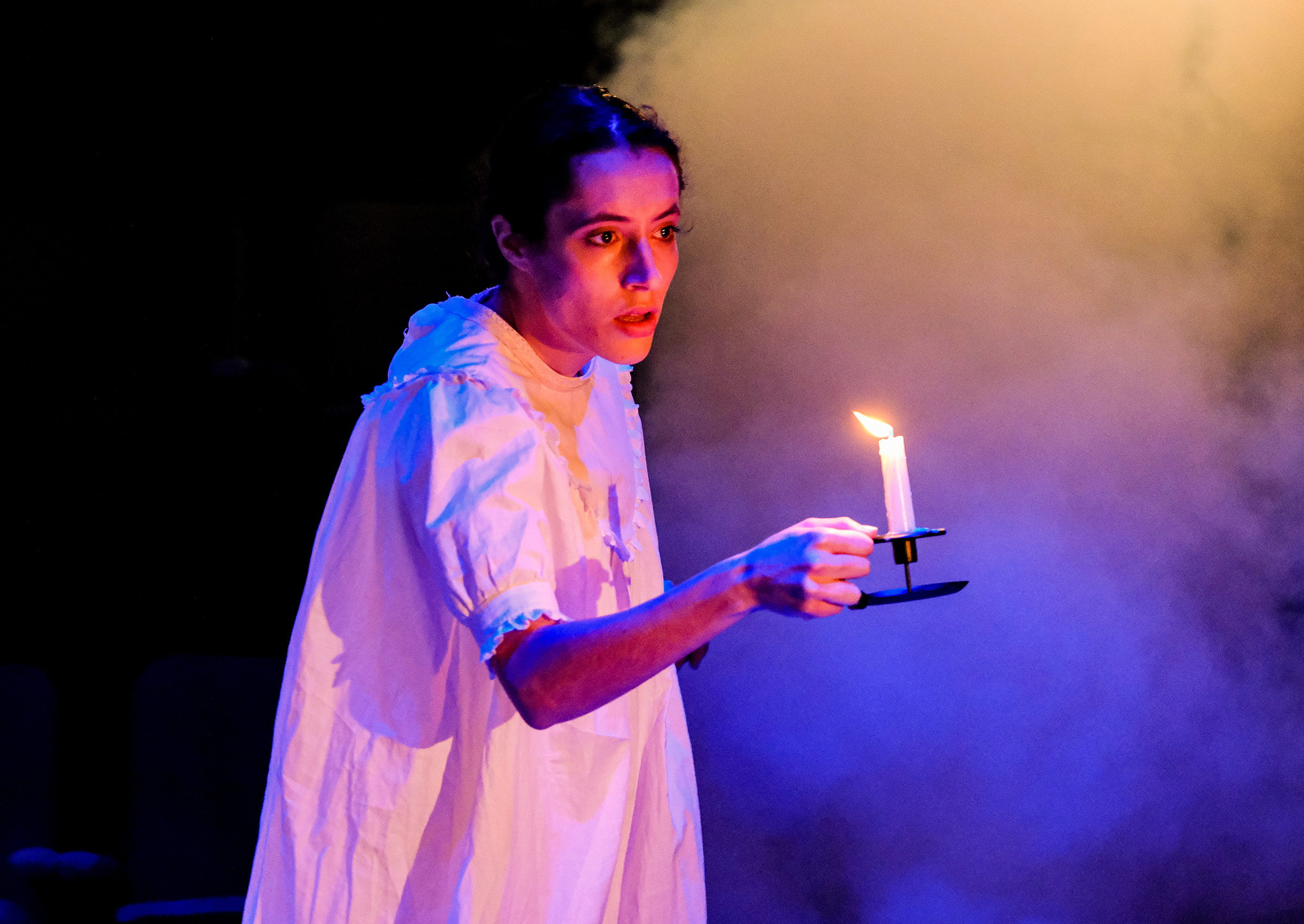 theatre performance image: Jane Eyre in a nightdress, holding a candle with smoke in the background