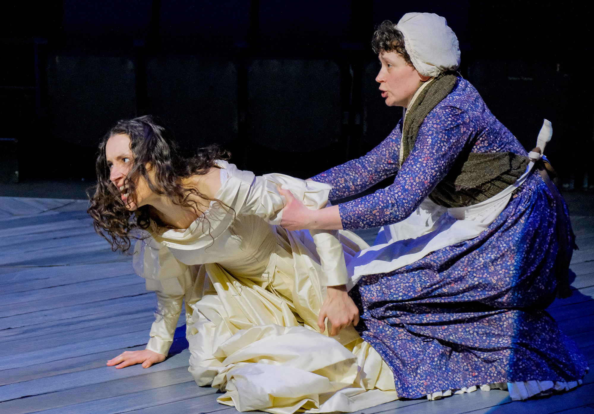 theatre performance image: a performer in a wedding dress is being held back by another in servant's clothes